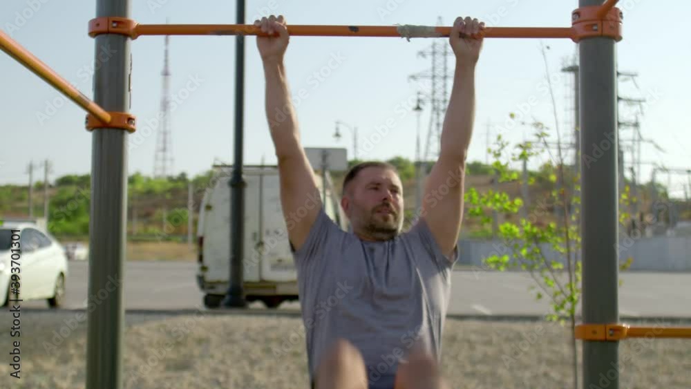 Senior sporty man hangs on a horizontal bar and raises his legs Senior sporty man hangs on a horizontal bar and raises his legs
