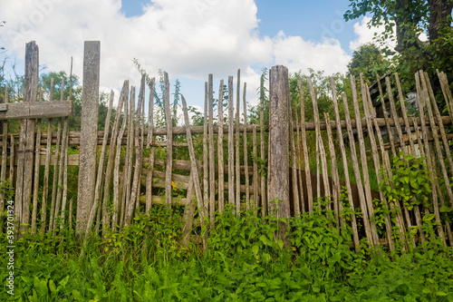 Old rickety wooden fence made of narrow boards in front of village house
