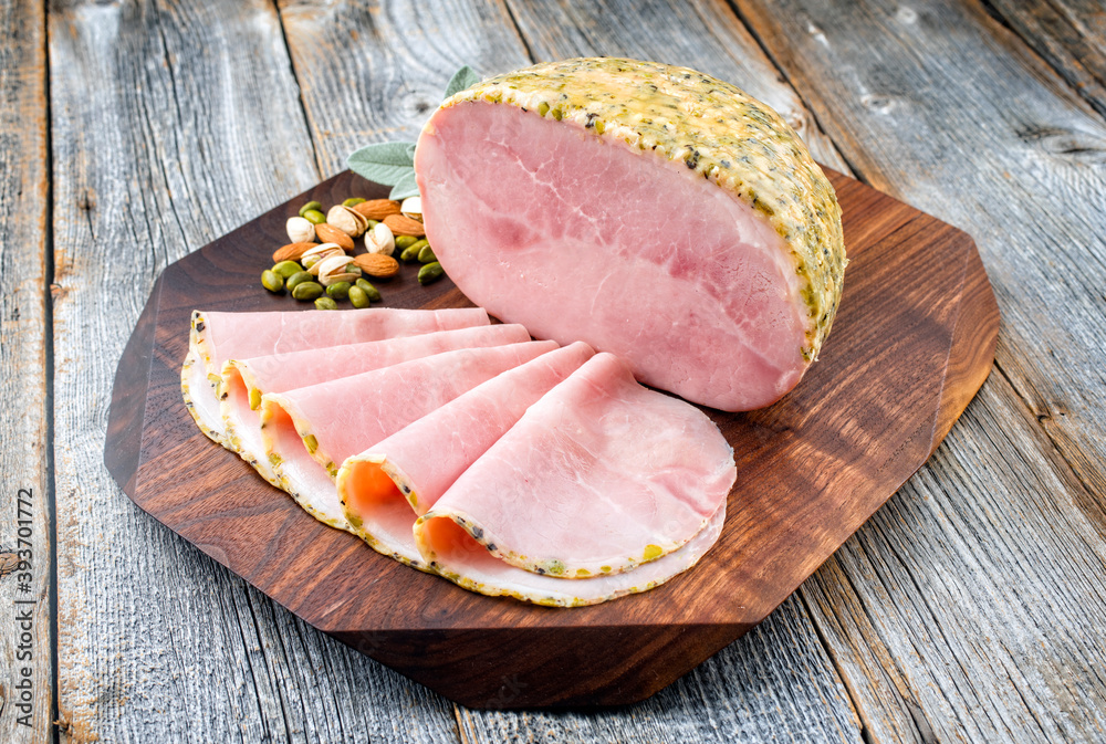 Modern style traditional German boiled Christmas ham with exotically spices and sage offered as close-up on a wooden design board with copy space