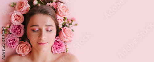 Fototapeta Naklejka Na Ścianę i Meble -  Close up portrait of beautiful woman face wih bright make up and perfect skin posing with roses on pink background.