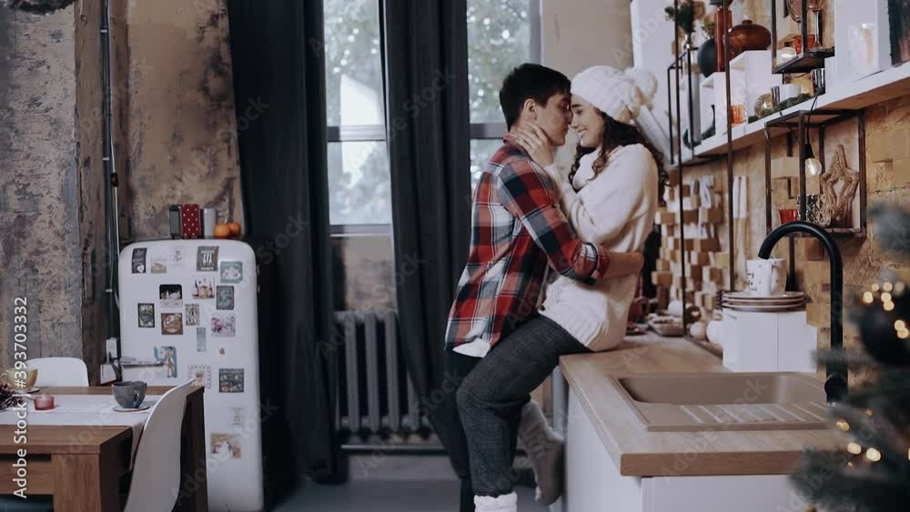 Young couple holding hands at home in the kitchen. Young people happily hug. Happy young people spend nice time at home on Christmas Eve. New Year 2020, pandemic holiday concept.