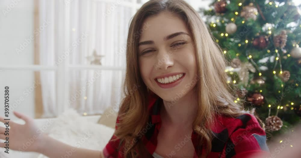 Close up of happy smiling Caucasian young woman speaking on video call at cozy home near glowing decorated xmas tree. Xmas greetings. Holiday congratulation. POV concept. Merry Christmas Close up of happy smiling Caucasian young woman speaking on video call at cozy home near glowing decorated xmas tree. Xmas greetings. Holiday congratulation. POV concept. Merry Christmas