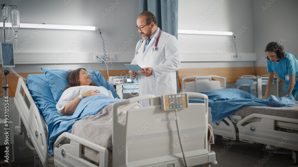 Hospital Ward: Friendly Latin Doctor Talks to Beautiful Female Patient Resting in Bed, Uses Tablet Computer, Explains Test Results. Physician Talks to Woman Recovering after Successful Surgery Hospital Ward: Friendly Latin Doctor Talks to Beautiful Female Patient Resting in Bed, Uses Tablet Computer, Explains Test Results. Physician Talks to Woman Recovering after Successful Surgery