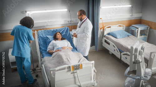 Hospital Ward  Friendly Latin Doctor Consulting Female Patient Resting in Bed. Physician Explains Test Results to Happy Woman Recovering after Successful Surgery. Nurse Checks Equipment. High Angle.