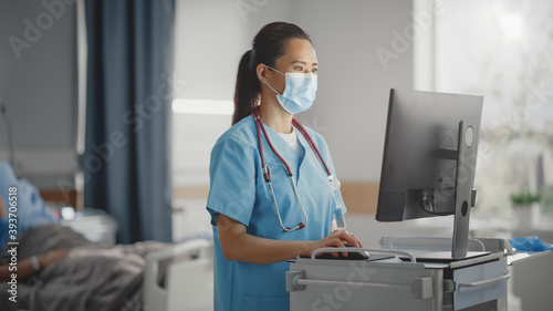 Fotografiet Hospital Ward: Professional Experienced Chinese Head Nurse / Doctor Wearing Face Mask Uses Medical Computer, Checking Patient's Medical Data