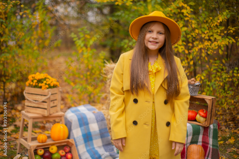 Obraz premium cute beautiful teenage brunette girl in an orange hat, dress and coat next to autumn decorations - pumpkins, apples, blankets, hay. Cosiness