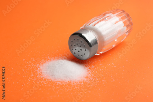 Scattered salt and shaker on orange background, closeup