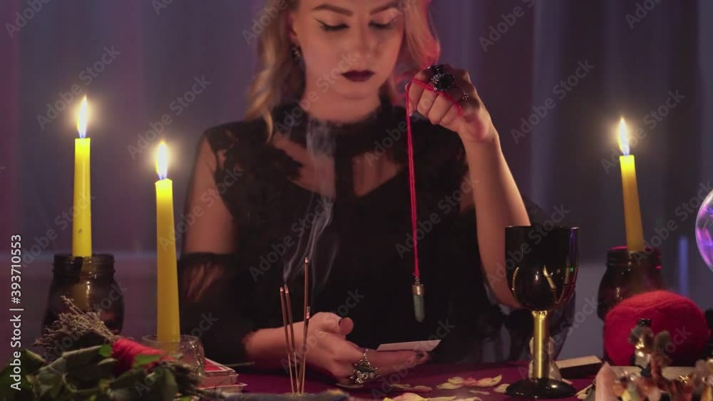 Female fortune teller holding a magic pendulum over a candle