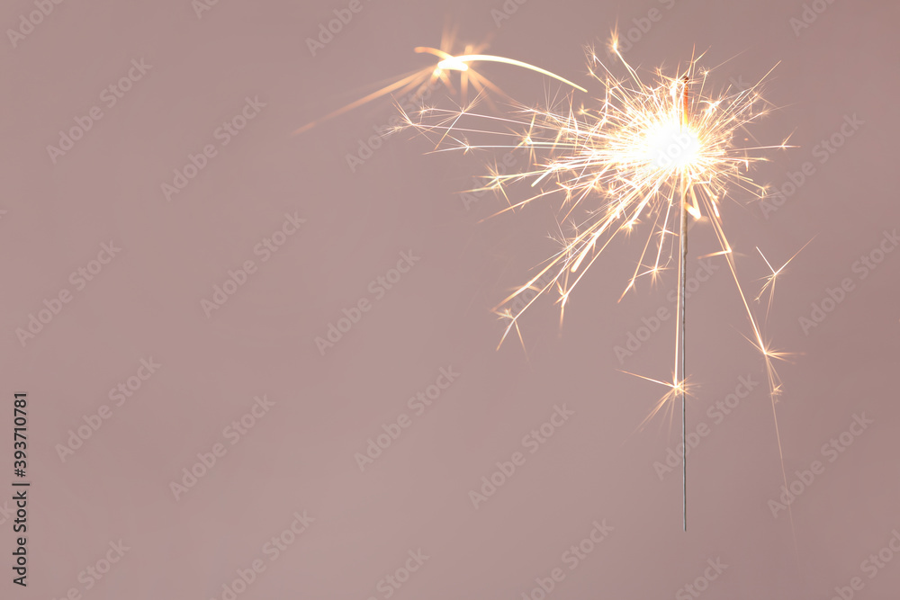 Bright burning sparkler on beige background, closeup. Space for text