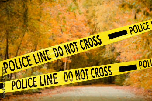 Yellow police tape isolating crime scene. Blurred view of autumn park