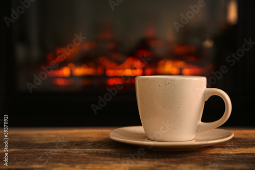 Cup with hot drink on table against fireplace, space for text