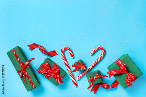 Christmas gift boxes with red bows and candy canes on light blue background, flat lay. Space for text