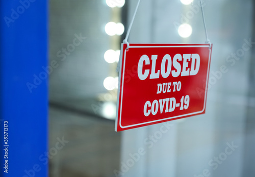 Red sign with text Closed Due To Covid-19 hanging on glass door, closeup. Coronavirus quarantine
