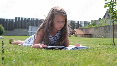 A girl reads a book in the garden on the grass.