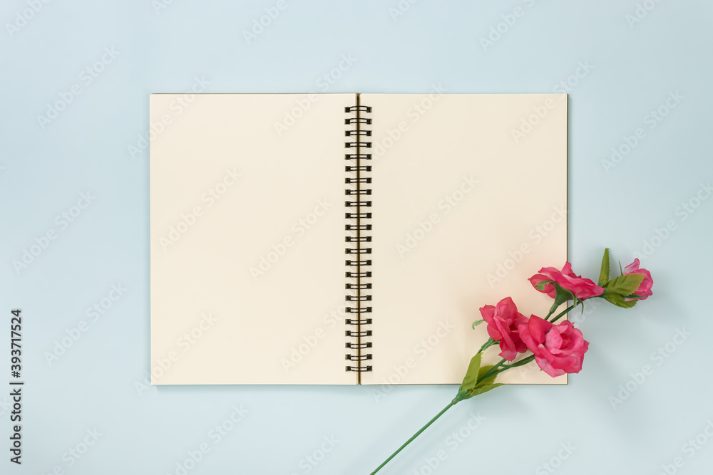 Top Table Spiral Notebook or Spring Notebook Mock up in Unlined Type on Center Frame and Rose Flowers at Bottom Right Corner on Blue Pastel Minimalist Background Top Table Spiral Notebook or Spring Notebook Mock up in Unlined Type on Center Frame and Rose Flowers at Bottom Right Corner on Blue Pastel Minimalist Background
