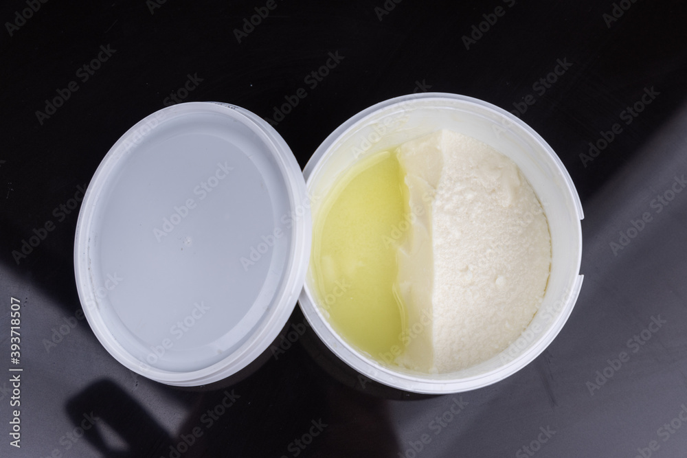 Layer of whey protein formed on top of packaged yogurt after opening in dark background. Layer of whey protein formed on top of packaged yogurt after opening in dark background.