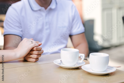 Marry me today and everyday. Close up picture of a couple's hand with golden rings holding each other, wedding picture. Two white coffee cups are on the wooden table. Selective Focus.