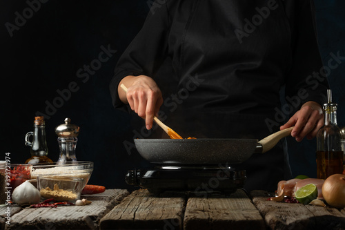 Professional chef stir ingredients in frying pan. Backstage of cooking traditional Indian chicken curry on dark blue background. Frozen motion. Concept cooking process. Frozen motion.