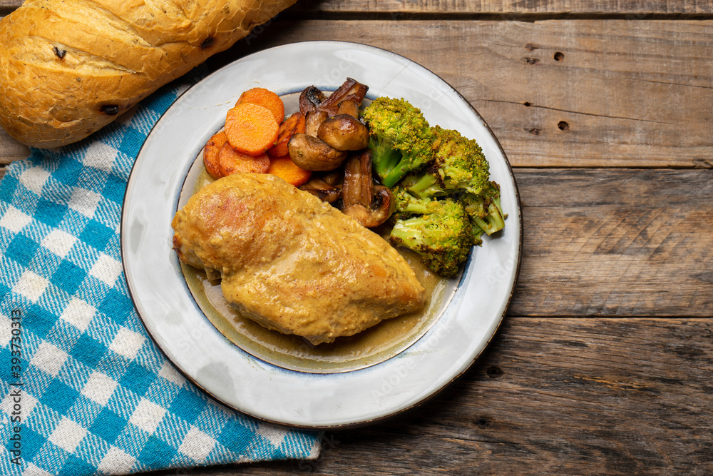 Chicken in mustard sauce with roasted vegetables in wooden background Chicken in mustard sauce with roasted vegetables in wooden background