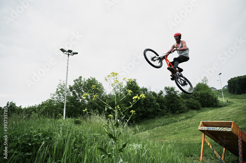 Young Caucasian man jumping on a mountain bike from a springboard in the forest.