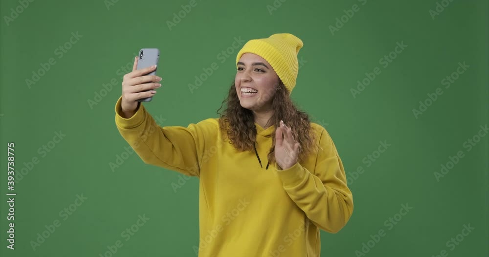 Happy woman in knit hat video chatting using mobile phone