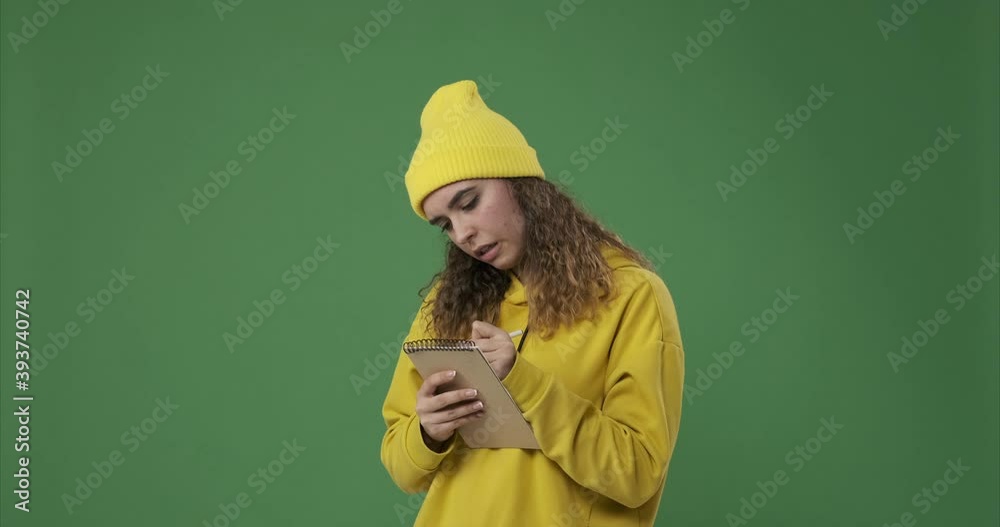 Thoughtful woman writing in notepad over green background