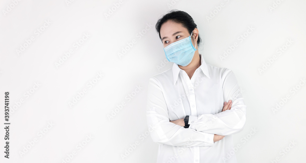 Asian woman in a white shirt standing with arms folded wearing a mask to protect against the corona virus or covid 19 on a white background with copy space Asian woman in a white shirt standing with arms folded wearing a mask to protect against the corona virus or covid 19 on a white background with copy space