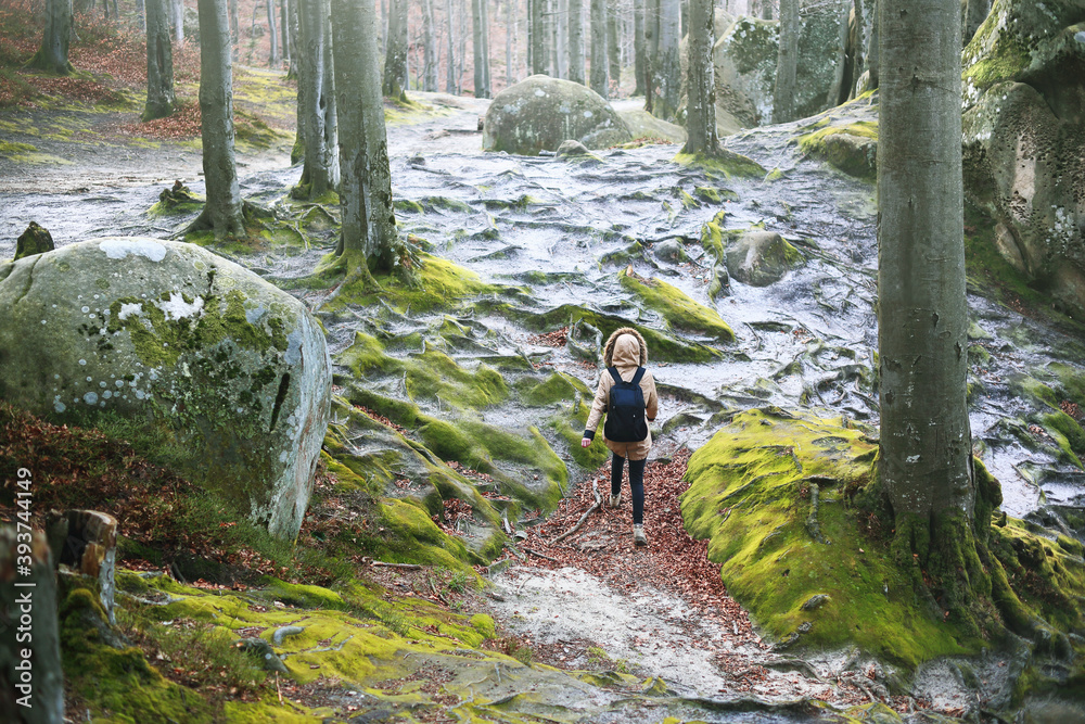 Young caucasian woman walks in a fabulous mountain forest between large rocks.