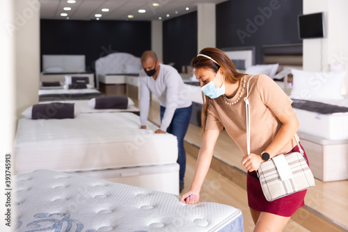 Fine couple wearing protective masks choosing a new mattress at a furniture store