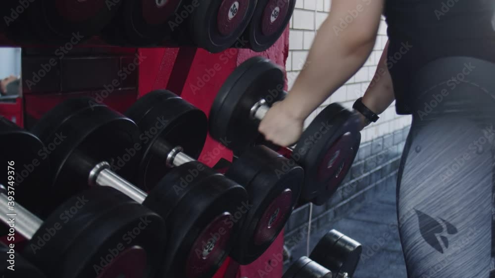 Close up of muscular womangirl chooses a dumbbell at gym Close up of muscular womangirl chooses a dumbbell at gym