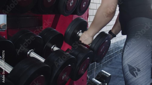 Close up of muscular womangirl chooses a dumbbell at gym photo