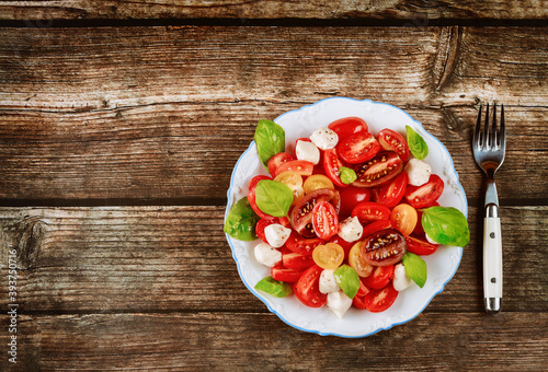 Tasty salad made from cherry tomato, mozzarella cheese and basil on white plate with fork.
