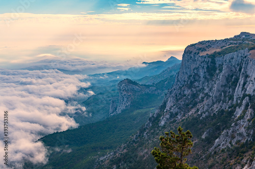 A majestic view of the rocky mountains and the valley in fog and clouds. Creamy fog covered the mountain valley in sunset light. Picturesque and gorgeous scene. Misty sunset over Crimea Mountains