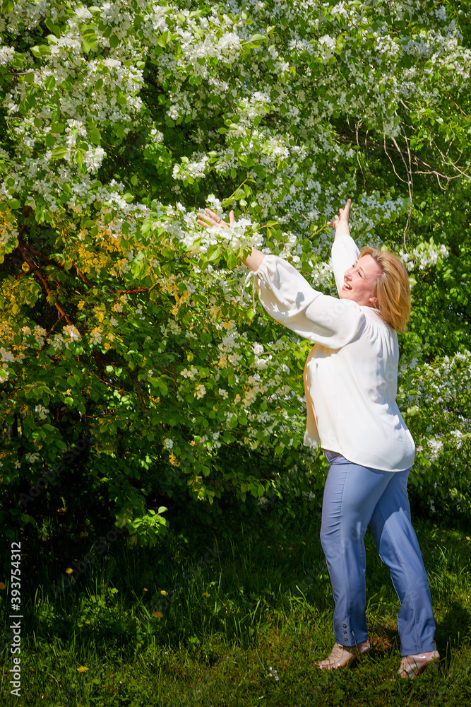 Outdoor portrait of a beautiful blonde middle-aged woman near blossom apple trees with white flowers. Outdoor portrait of a beautiful blonde middle-aged woman near blossom apple trees with white flowers.