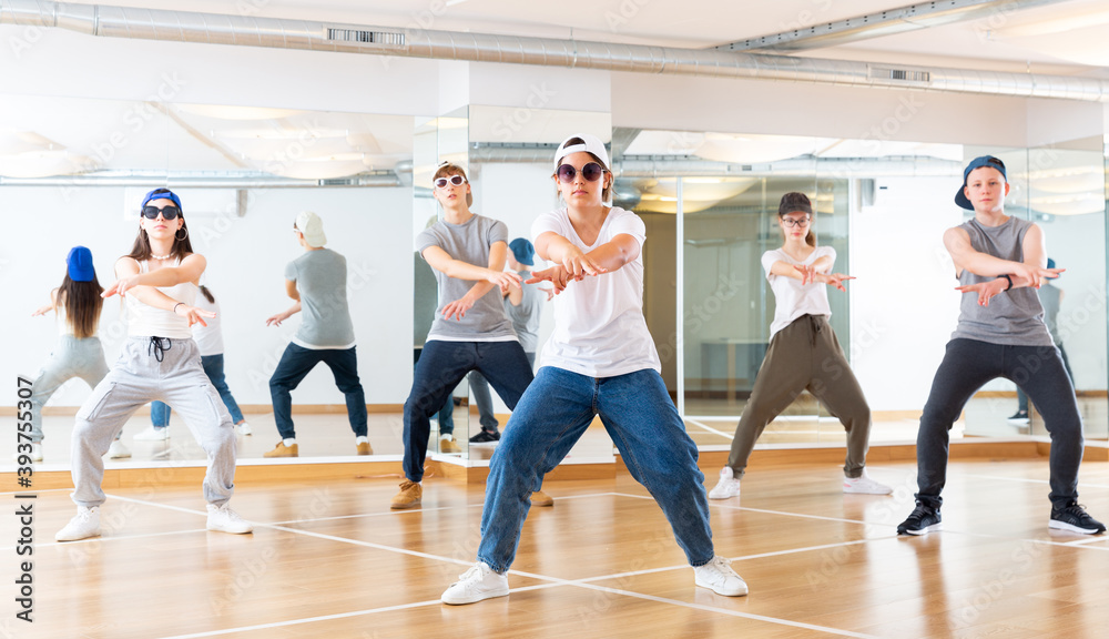 Group of teenagers in casual clothes training hip-hop in class, learning modern dance movements