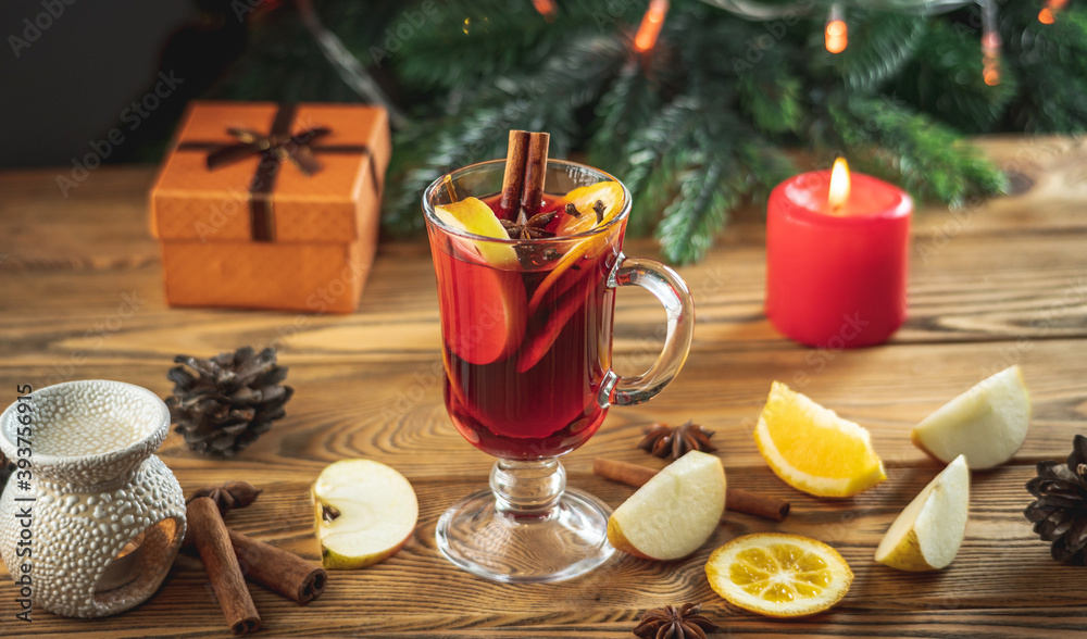 Cup of aromatic hot mulled wine on a wooden table on the background of a Christmas tree with lights. Concept of a festive atmosphere