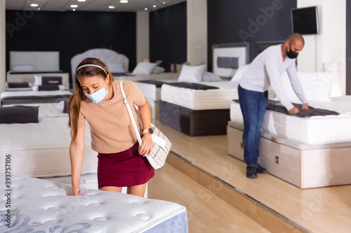 Couple in protective masks choosing a new mattress at a furniture store