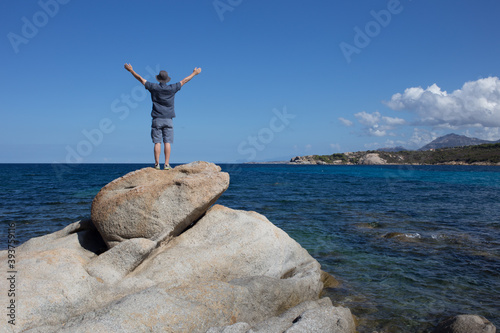 Man Standing on a Rock with Outstretched Arms on the Coast of Corsica, France Overlooking the Mediterranean Sea