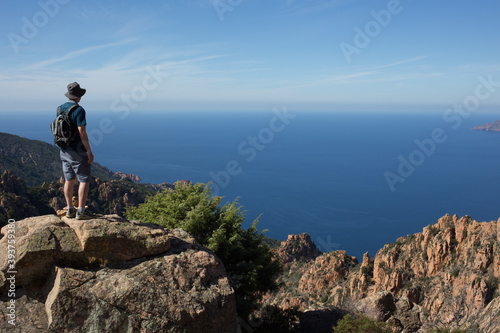 Man Standing at the Edge of a Rocky Cliff Overlooking the Mediterranean Sea from the Island of Corsica, France 