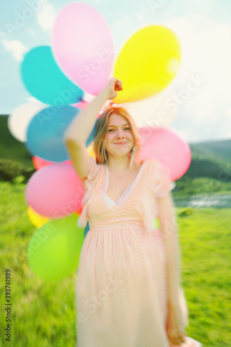 Young caucasian woman in a dress with balloons in hands in the mountains.