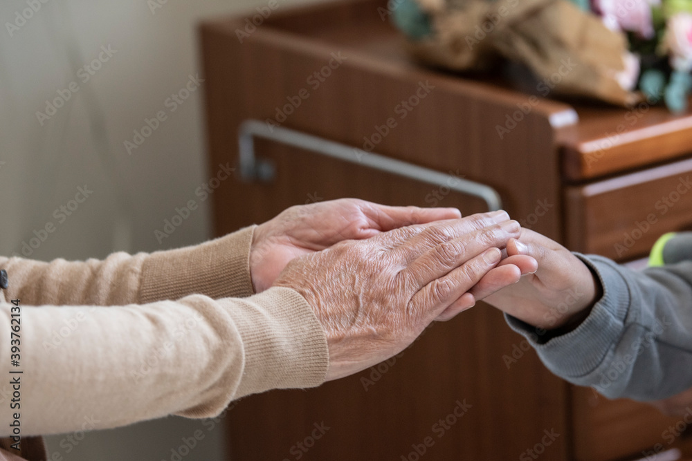 入院中のおばあちゃんとお見舞いに来た孫が手をつないでいる
