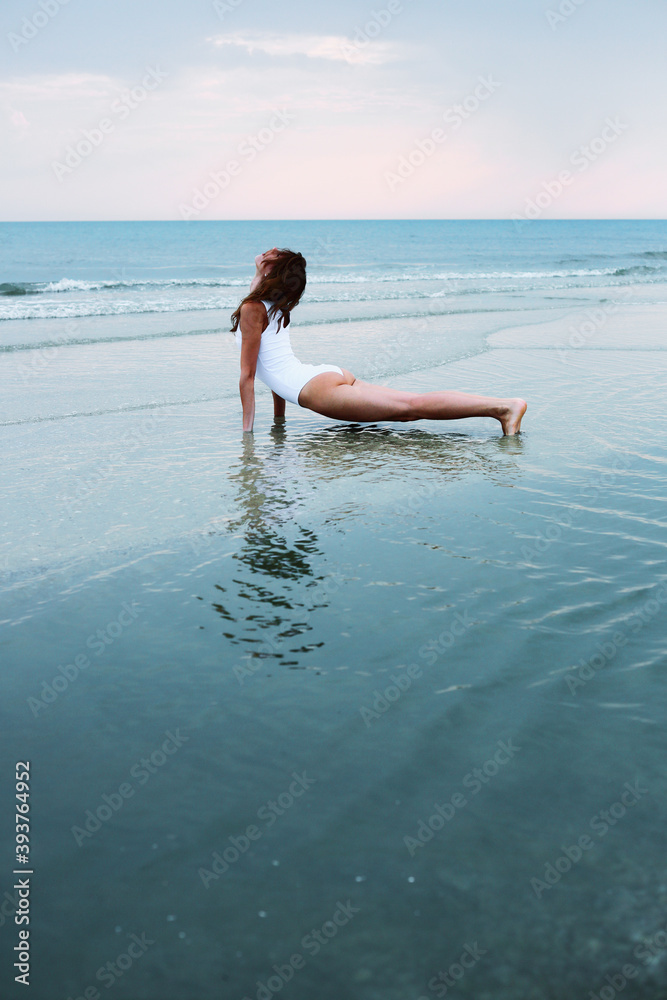 Young caucasian woman doing yoga in sea water on the coast.