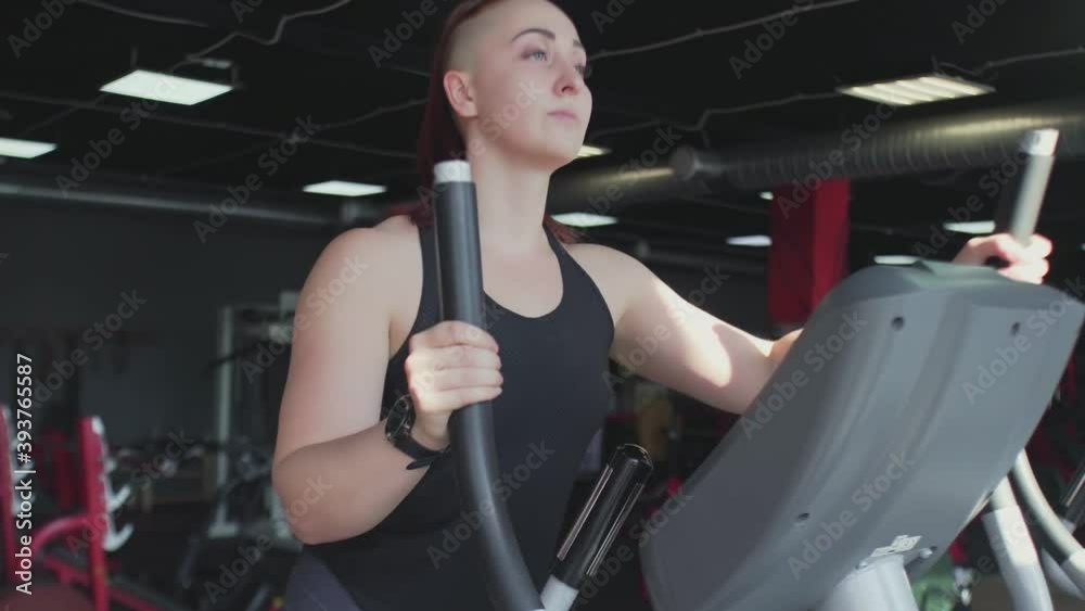 Muscular woman warms up on Elliptical Machine before training