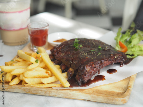 Pork Spareribs BBQ, Barbeque Pork Ribs with french fries vegetable salad, tomato sauce in a clear glass on wooden tray, food delicious