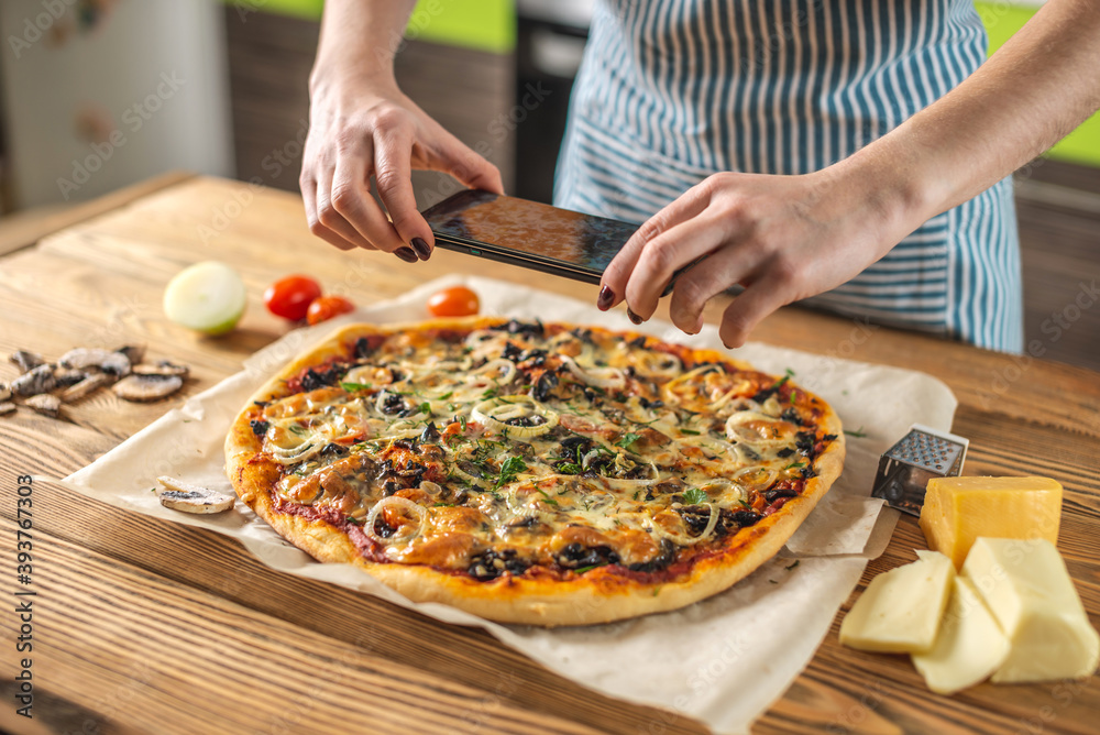 Female chef blogger takes photos of home-made pizza on her phone. The concept of food photography for social networks