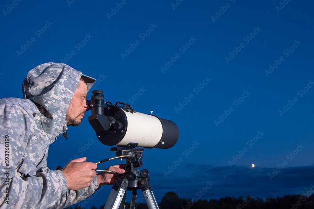 A male astronomer observes the sky through a telescope. Amateur astronomy concept.