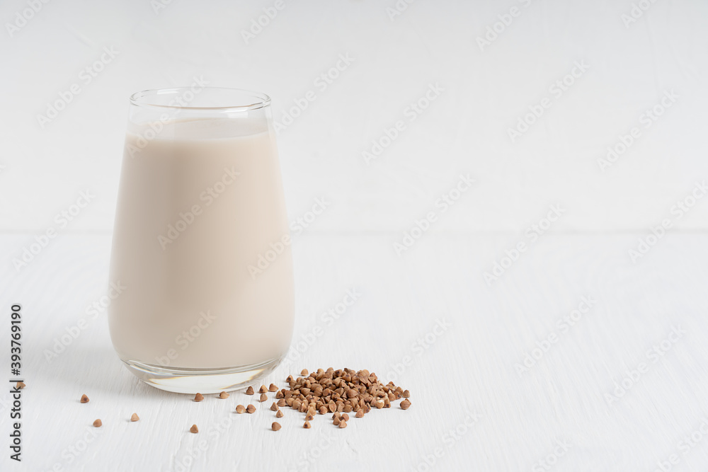 Gluten-free and lactose-free healthy buckwheat milk full of vitamins, minerals and antioxidants served in tall drinking glass with raw grains on white wooden background. Image with copy space Gluten-free and lactose-free healthy buckwheat milk full of vitamins, minerals and antioxidants served in tall drinking glass with raw grains on white wooden background. Image with copy space