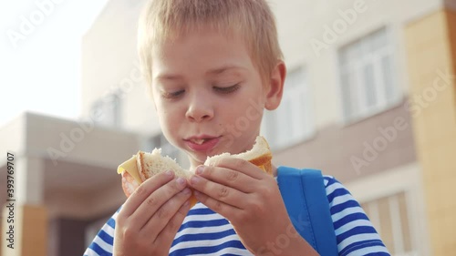 schoolboy eating a sandwich during recess in school. kids education concept. little kid boy schoolboy with a backpack eating a sandwich. kid child is having lunch at lifestyle school photo