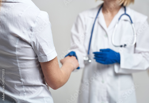 The nurse shakes hands with the patient on a light background and blue gloves with a stethoscope