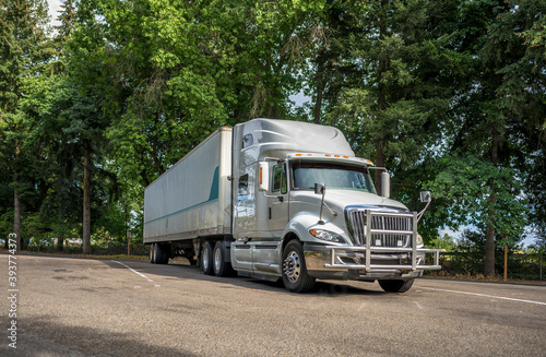 Big rig heavy long haul semi truck with dry van semi trailer standing on rest area parking lot in forest line